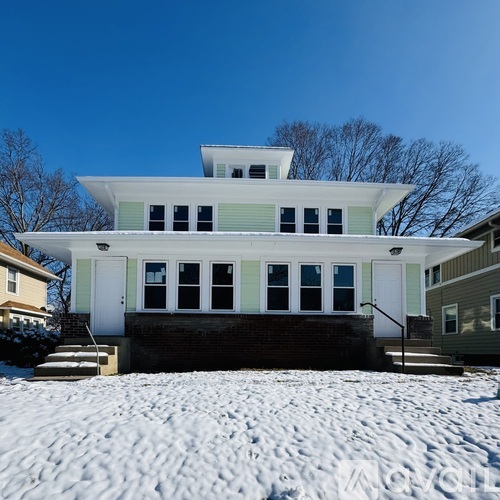 A white house with a green trim is surrounded by snow.