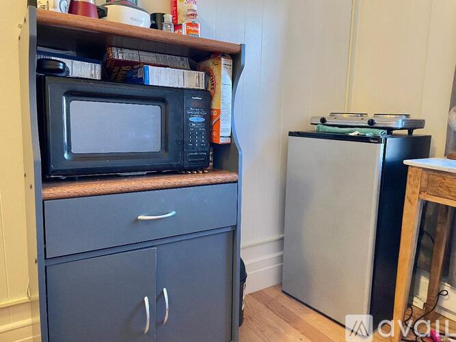 A black microwave oven is on a wooden shelf above a grey cabinet.