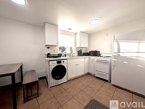 A kitchen with white appliances and brown tile flooring.