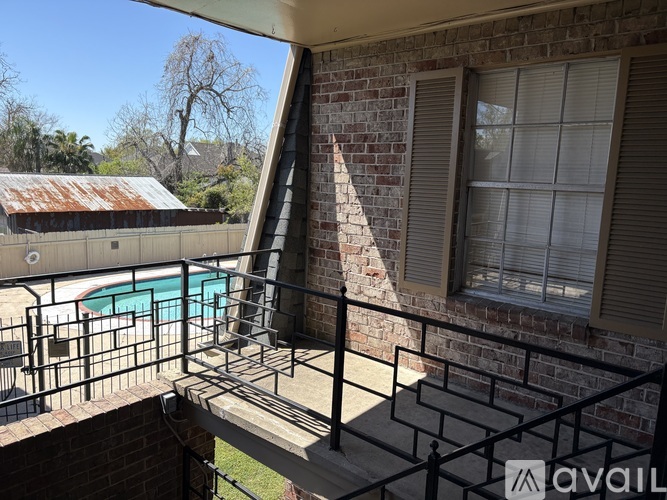 A balcony with a brick wall and a window overlooking a pool.