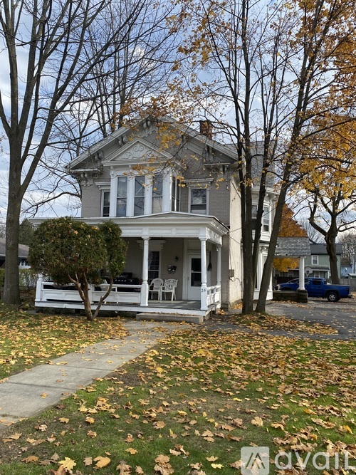 A house with a porch and a tree with yellow leaves in front of it.