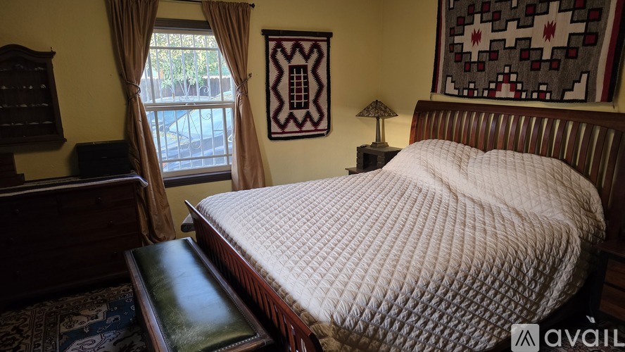 A bed with a white comforter sits in a room with a window and a lamp.