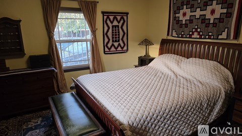 A bed with a white comforter sits in a room with a window and a lamp.