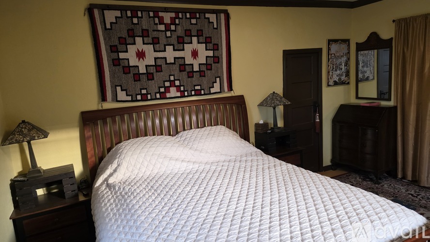 A bed with a white comforter and a wooden headboard with a patterned pillow.