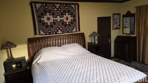 A bed with a white comforter and a wooden headboard with a patterned pillow.
