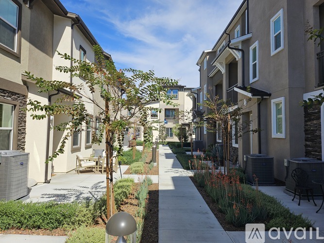 A row of modern townhouses with a sidewalk and landscaping.