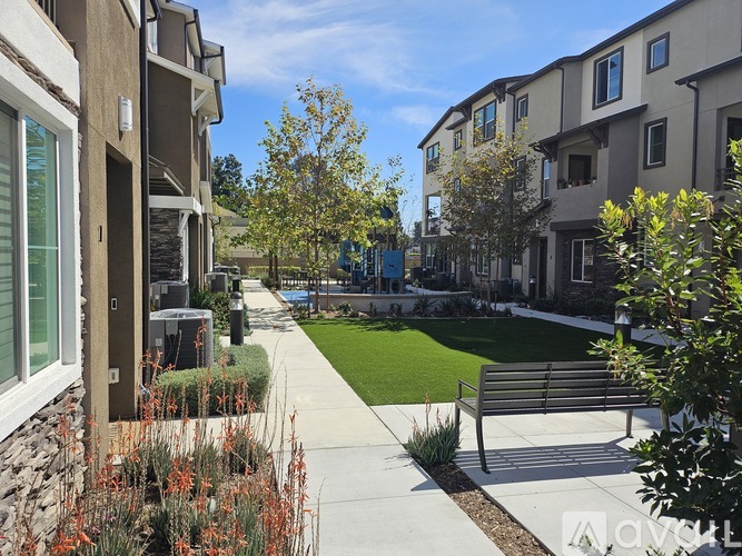 A row of apartment buildings with a sidewalk and bench in front.