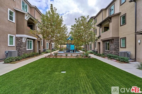 A well-maintained grassy area in front of apartment buildings with a playground in the middle.