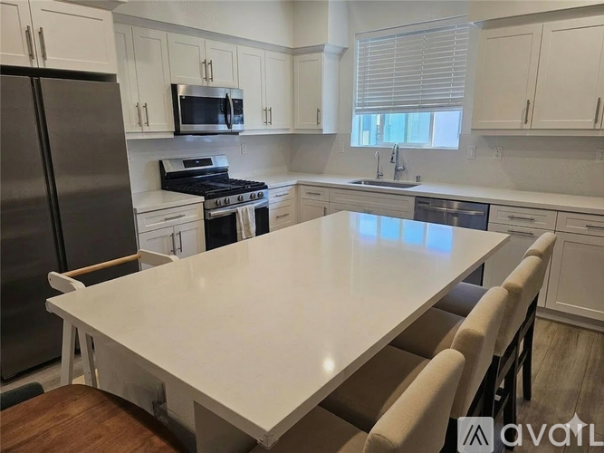 A kitchen with a table and chairs in the foreground and a refrigerator, microwave, and oven in the background.
