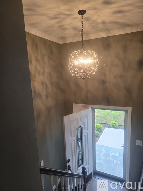 A chandelier hangs from the ceiling in a room with a view of a landscaped yard.