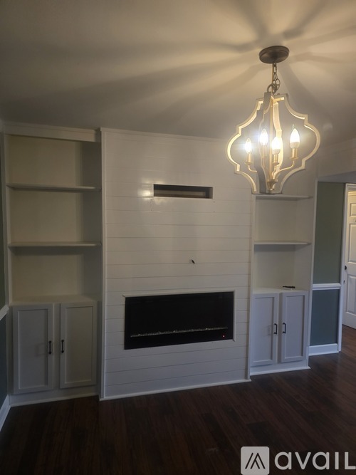 A chandelier hangs over a fireplace in a room with wood floors and white walls.