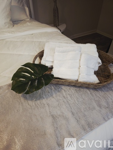 A basket of white towels and a green leaf on a bed.
