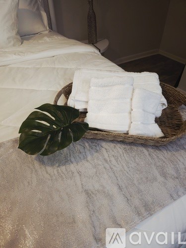 A basket of white towels and a green leaf on a bed.