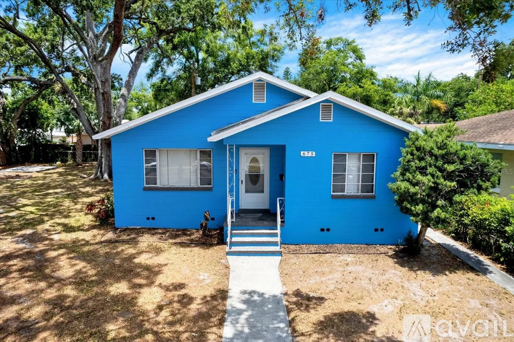 A blue house with a white door and windows is surrounded by trees.