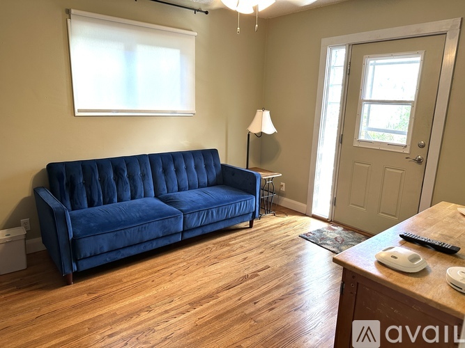 A blue velvet sofa sits in a room with wooden floors and a window.