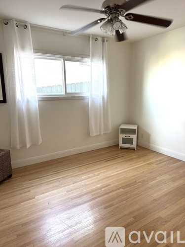 A room with a fan, a window with curtains, and a small table with a device on it.