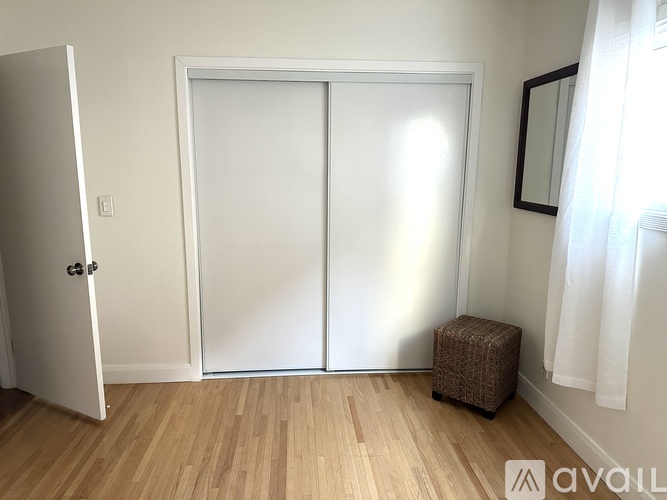 A room with a white door, a brown ottoman, and a white wall.