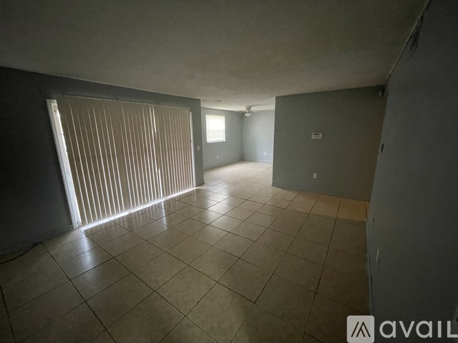 A spacious room with tiled flooring and a window with vertical blinds.