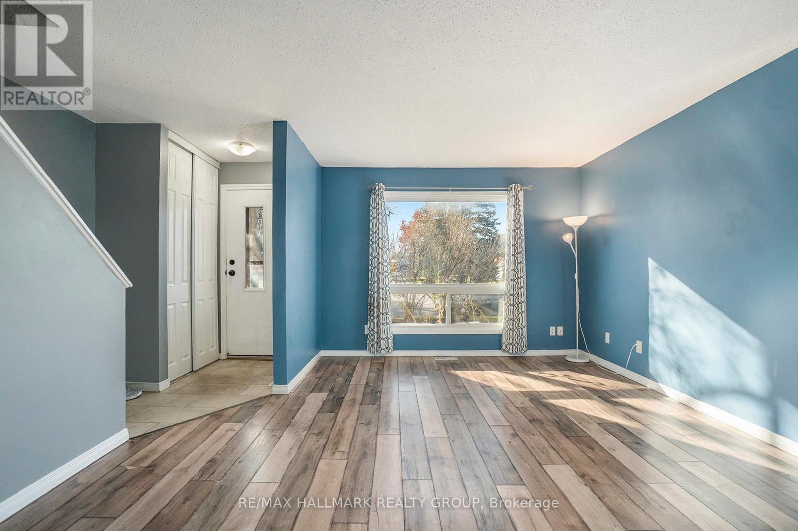 A spacious room with wooden floors and a view of trees through a large window.
