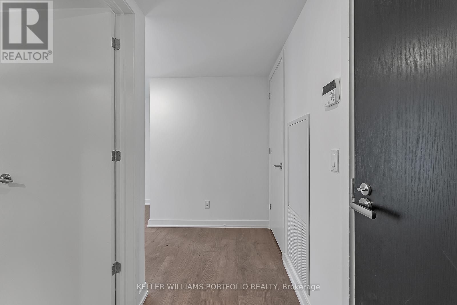 A hallway with a door on the right and a wall-mounted thermostat.