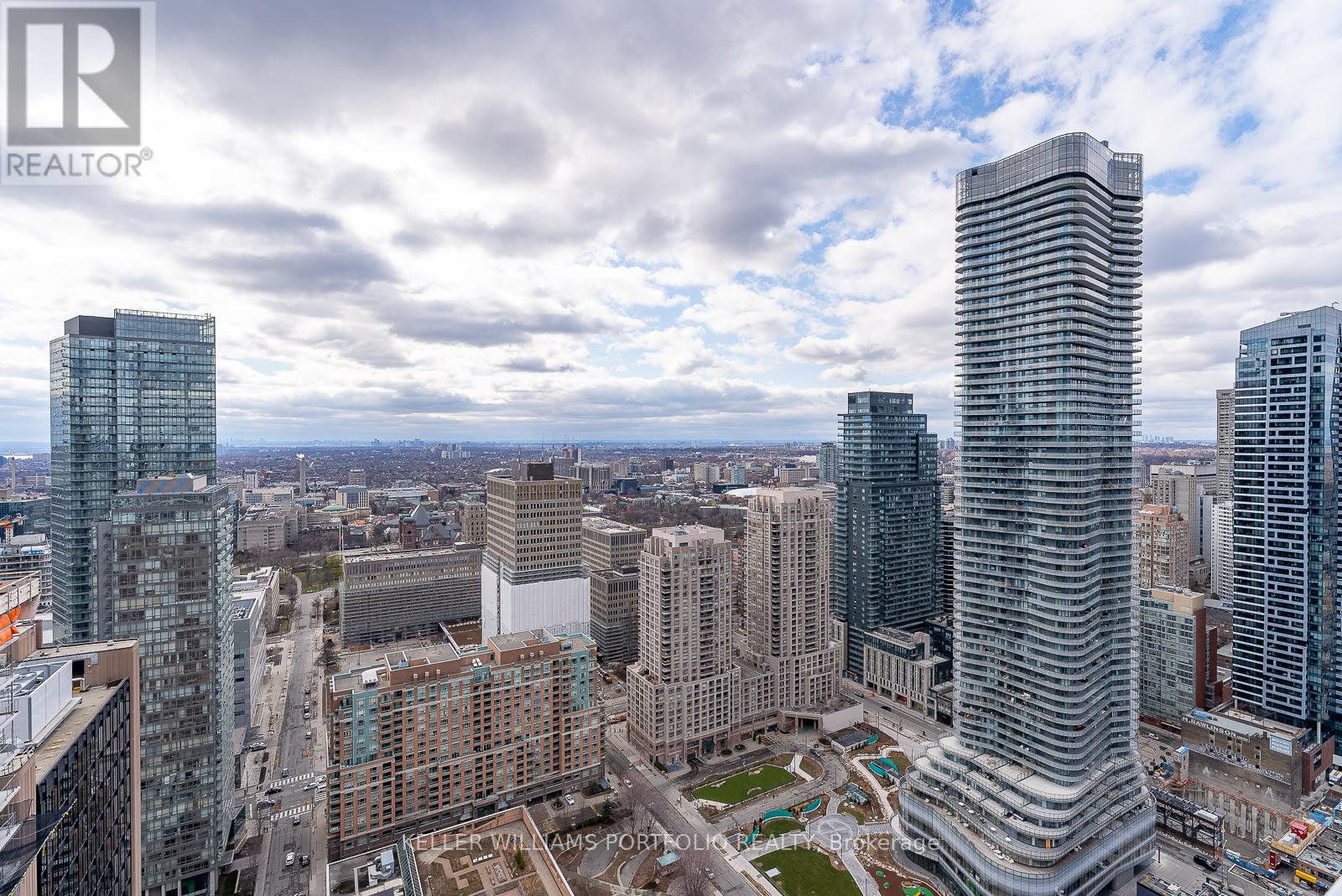 A cityscape with a tall building in the foreground and a cloudy sky above.