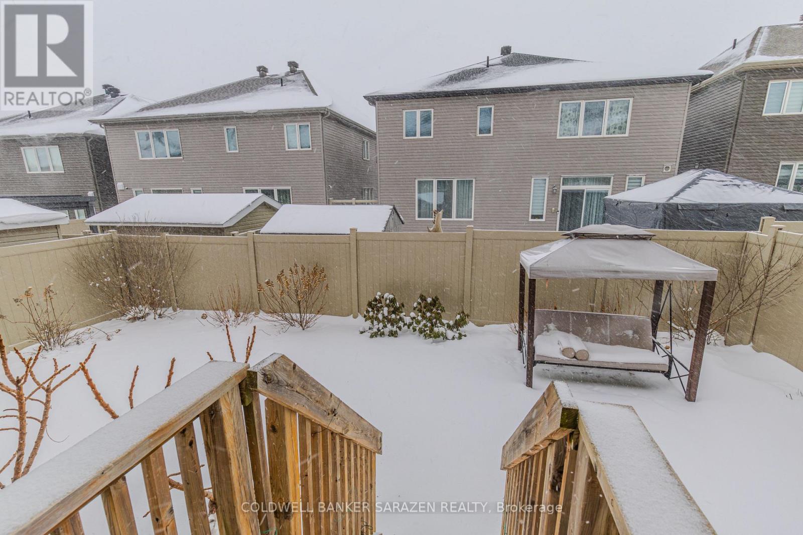 A snowy backyard with a wooden deck and a gazebo.
