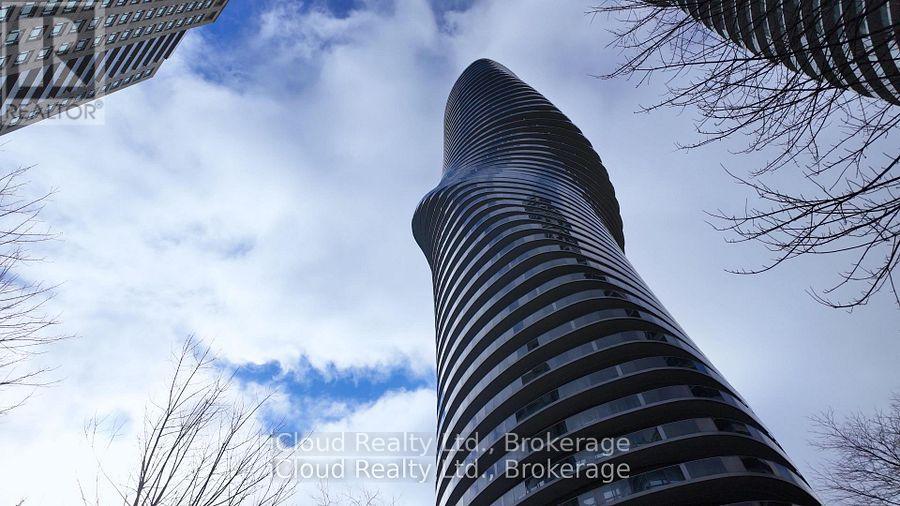 A tall, modern building with a curved facade stands against a cloudy sky.