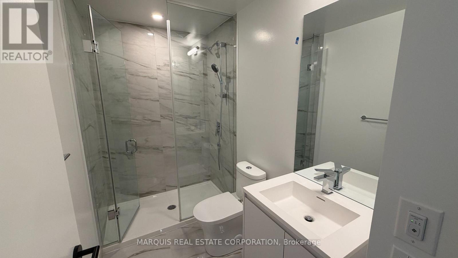 A bathroom with a glass shower stall and a white toilet.