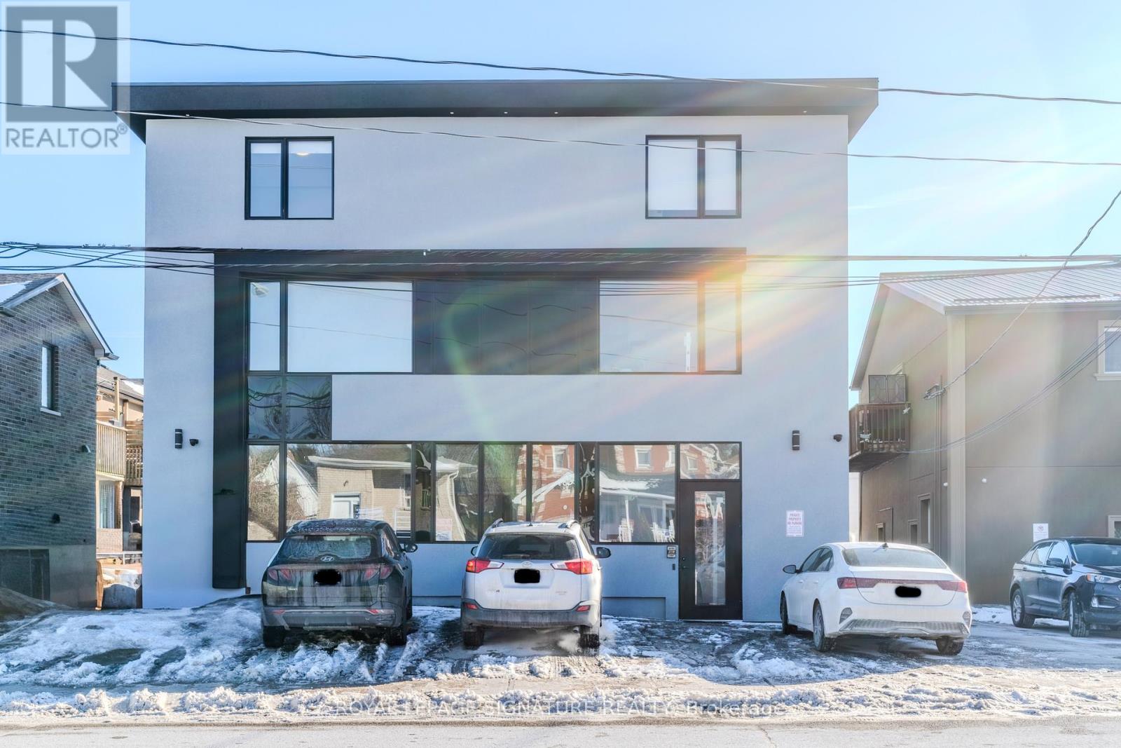 A modern house with a white and black exterior and a large glass window is shown with three cars parked in front.