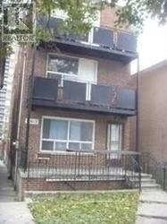A brown brick house with a white window and a black iron fence.