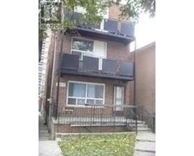 A brown brick house with a white window and a black iron fence.