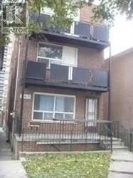 A brown brick house with a white window and a black iron fence.