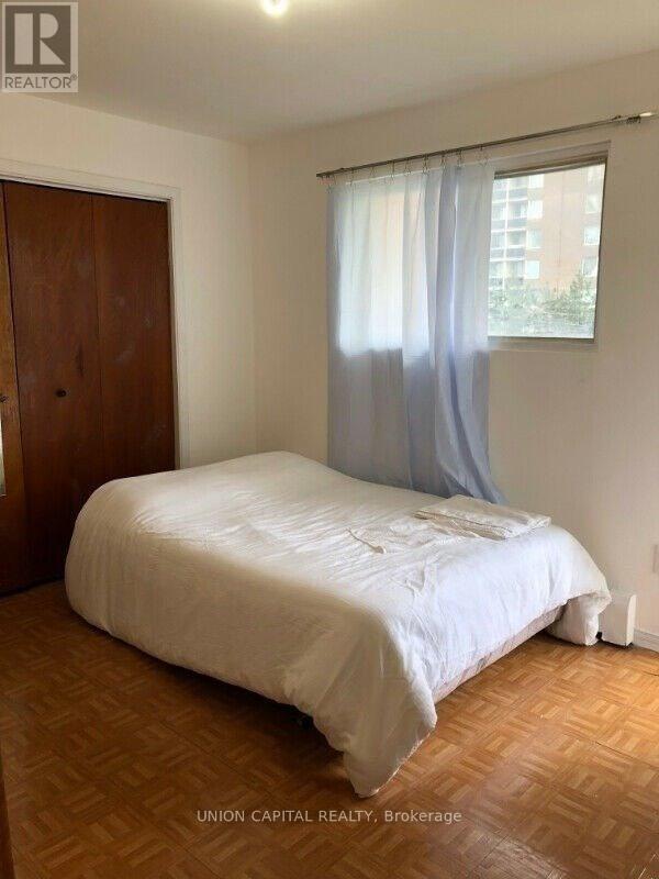 A bedroom with a bed, wooden floor, and a window with curtains.
