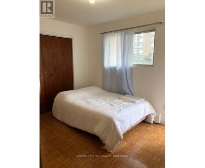 A bedroom with a bed, wooden floor, and a window with curtains.