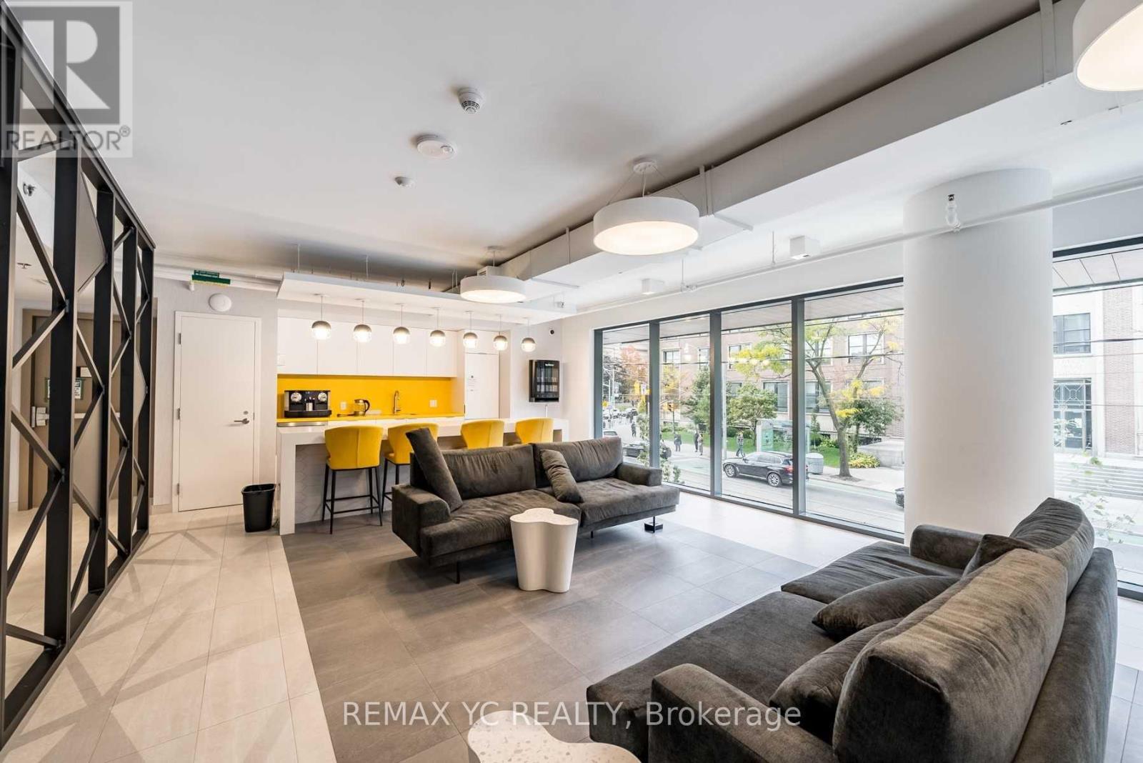 A modern living room with a grey couch and a yellow kitchen in the background.