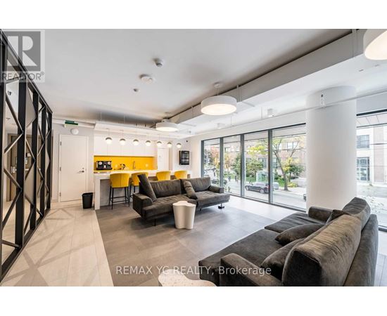 A modern living room with a grey couch and a yellow kitchen in the background.