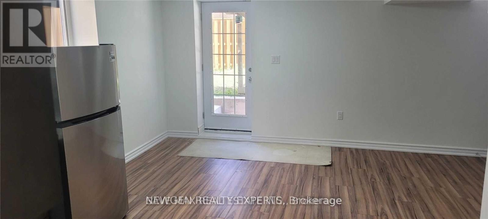 A room with a wooden floor and a white wall with a doorway leading to a balcony.