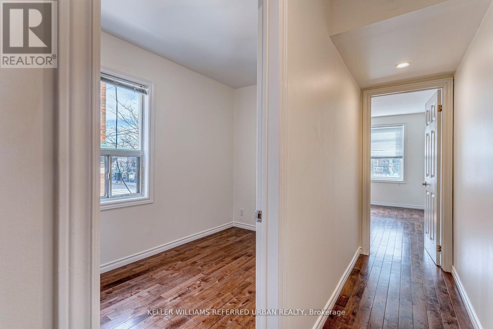 A room with wooden floors and white walls, with a window and a door visible.