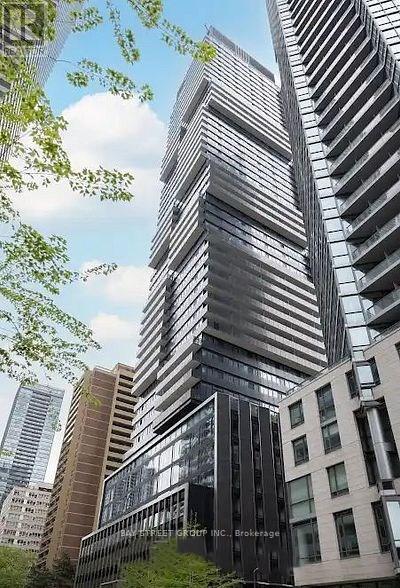 A tall building with a glass facade stands in front of other buildings.