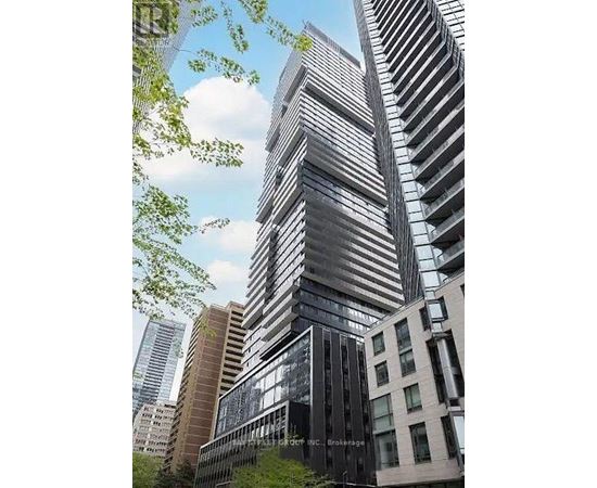 A tall building with a glass facade stands in front of other buildings.