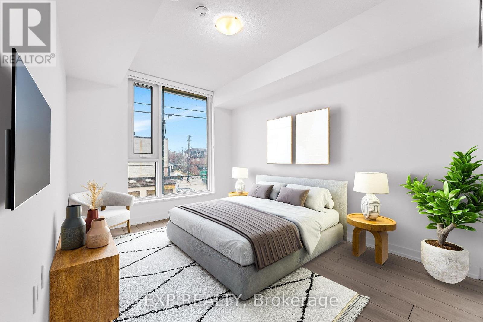 A well-lit bedroom with a large bed and a flat-screen TV mounted on the wall.