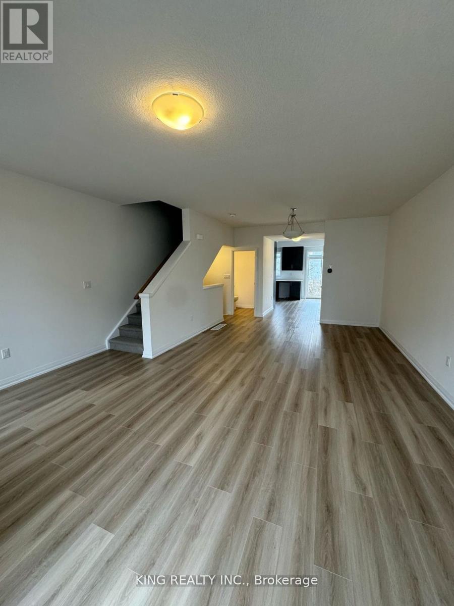A spacious room with wooden flooring and a staircase in the background.
