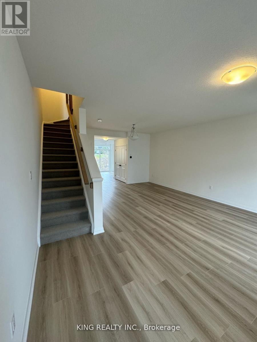 A spacious room with wooden flooring and a staircase leading to another room.