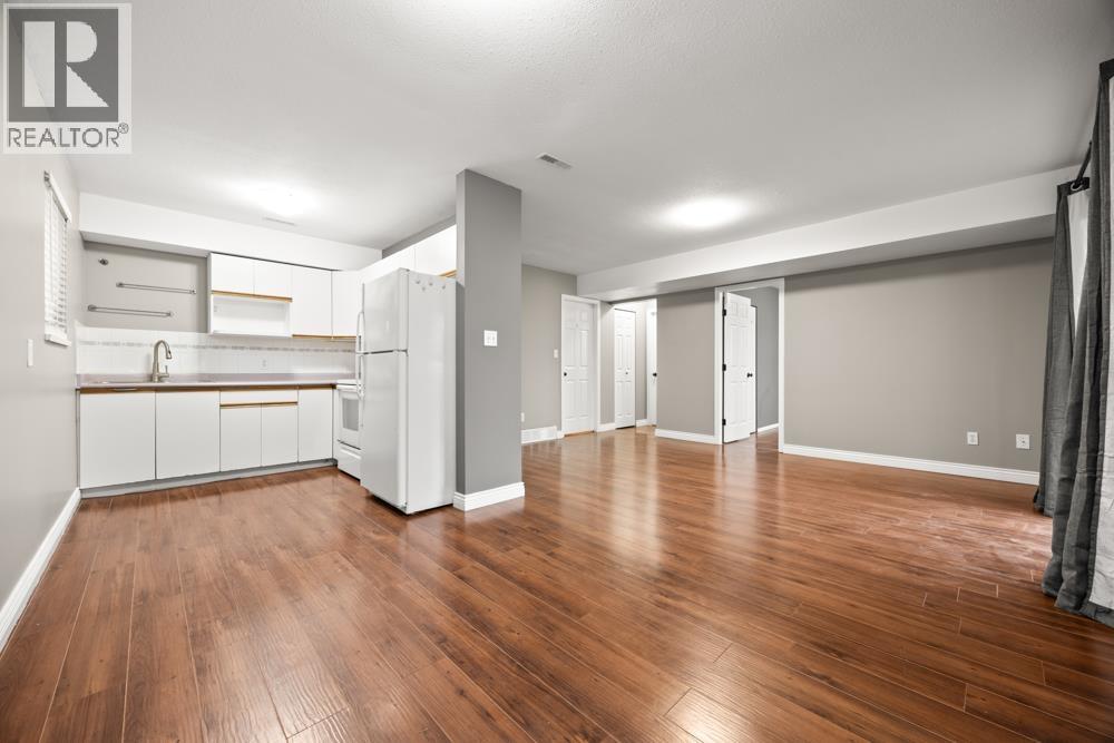 A large empty room with wooden floors and a kitchen area to the left.