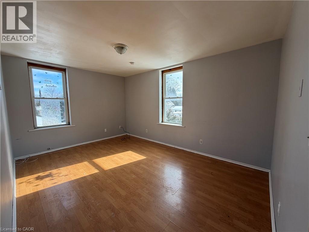 A room with wooden flooring and two windows.