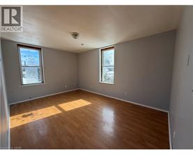 A room with wooden flooring and two windows.