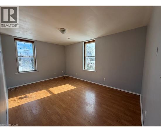 A room with wooden flooring and two windows.