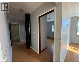 A room with a wooden floor and white walls, with a door open to another room.