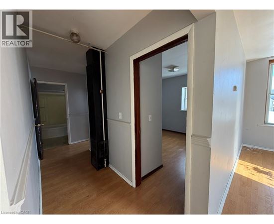 A room with a wooden floor and white walls, with a door open to another room.