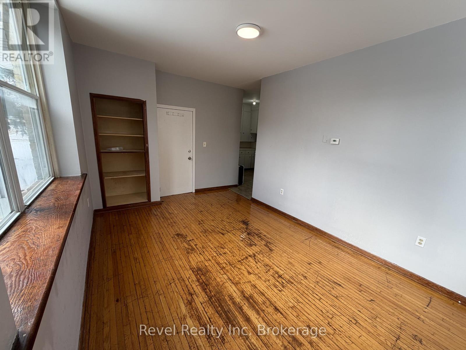 A room with wooden floors and white walls, with a window on the left side.